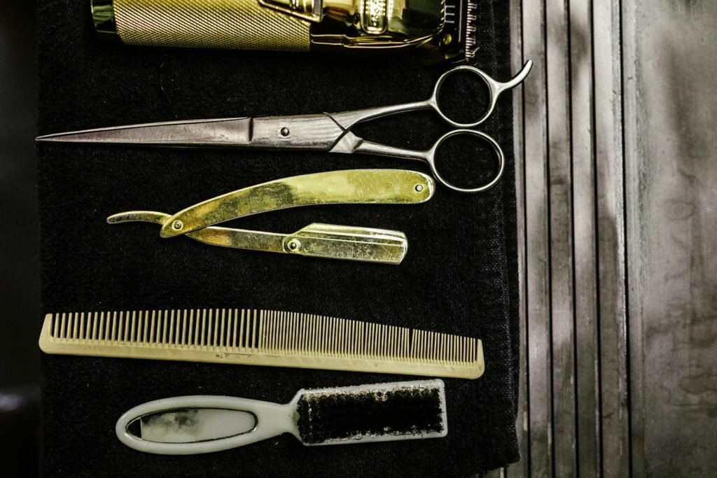 A set of vintage barber tools including scissors, razor, comb, and brush on a dark background.